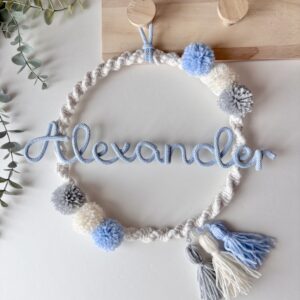 Personalized baby name wreath wall decor with soft pom poms hanging in neutral nursery room