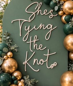 She’s tying the knot bachelorette party sign displayed on green arch with gold and dark green balloon garland