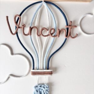 Personalized hot air balloon name sign handmade with cotton cord, displayed as nursery wall decor in a baby room.