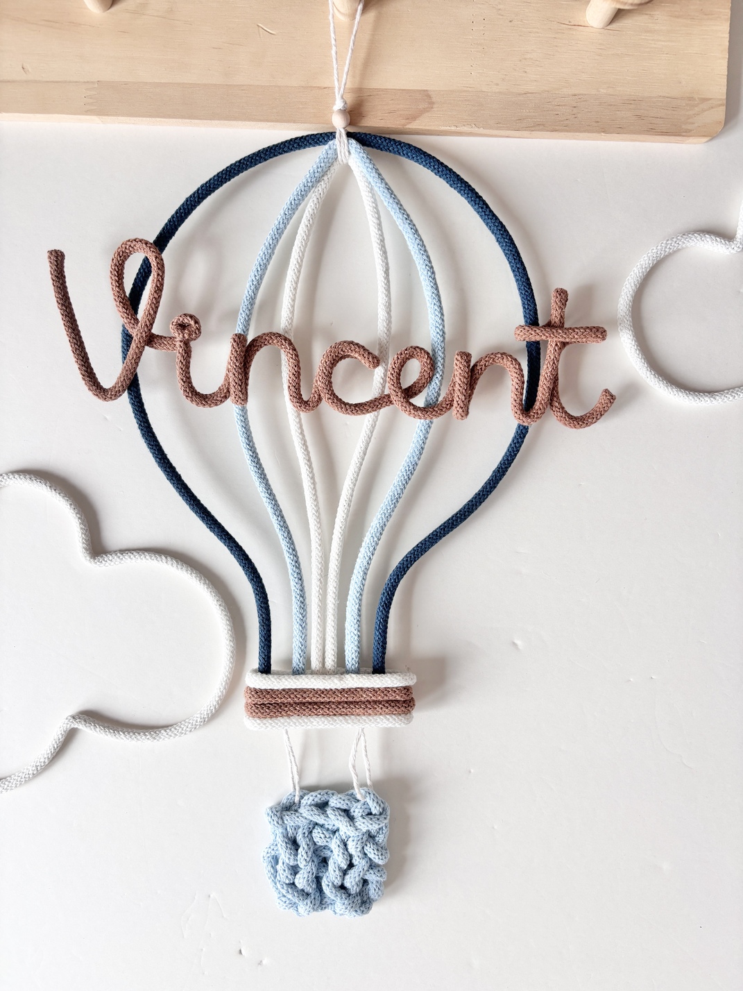 Personalized hot air balloon name sign handmade with cotton cord, displayed as nursery wall decor in a baby room.