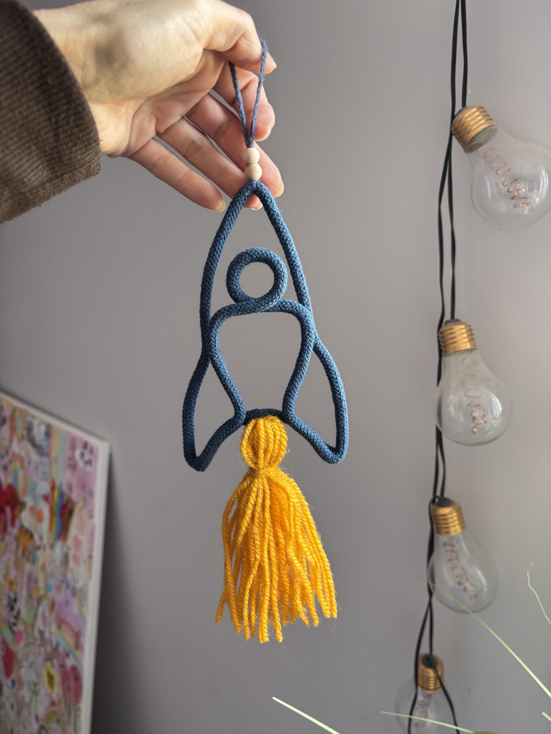Space rocket wall hanging for kids room decor, with a blue rocket shape and long golden tassel.