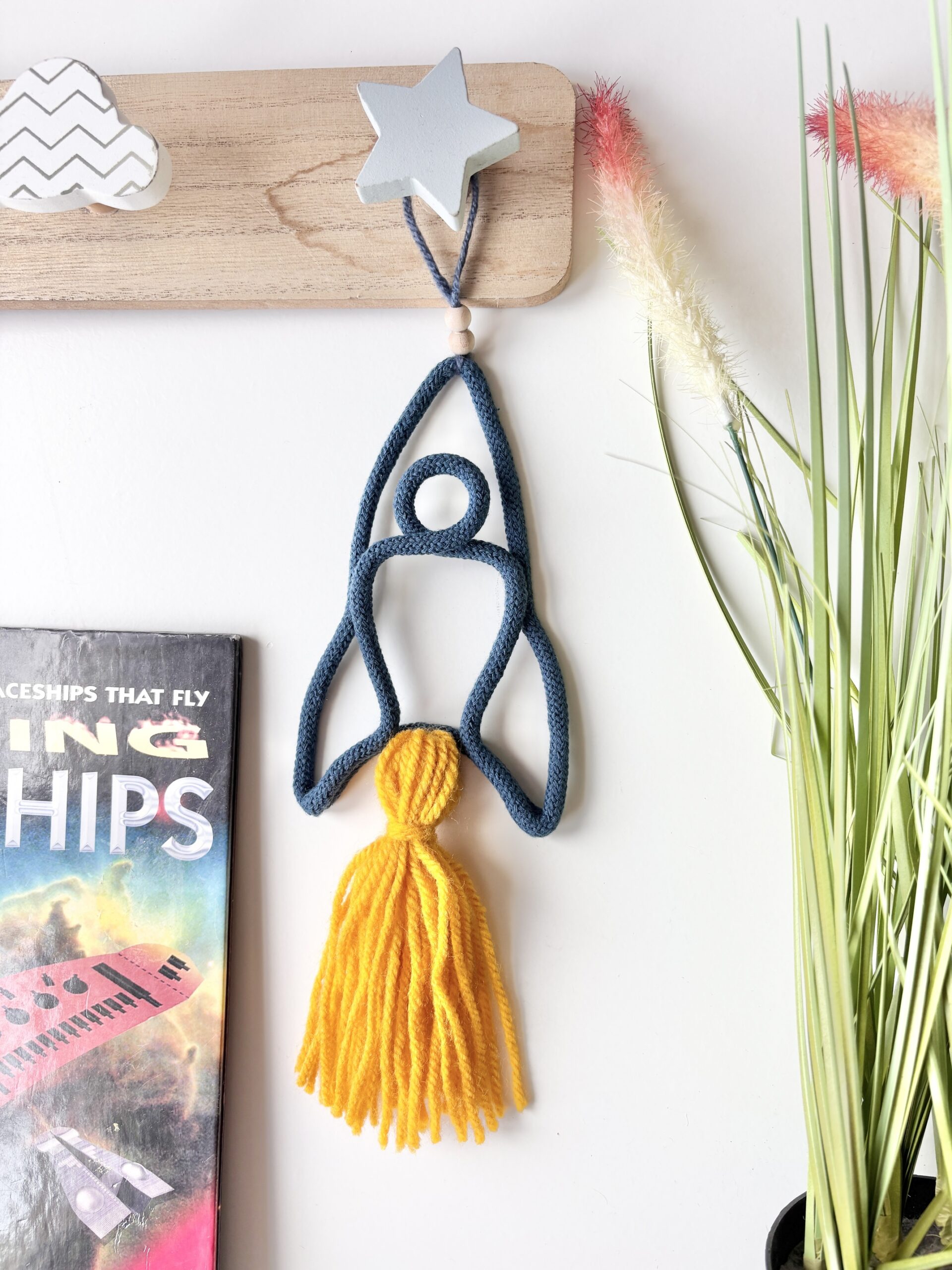 Handmade blue space rocket wall decor for a child's bedroom, featuring a golden tassel.