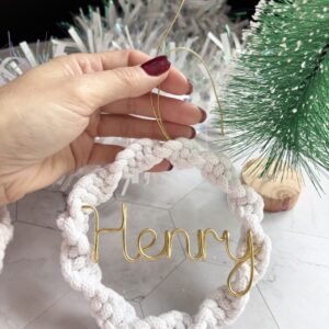Personalised Christmas tree ornament featuring a white textured wreath and elegant gold wire name lettering, held in hand.