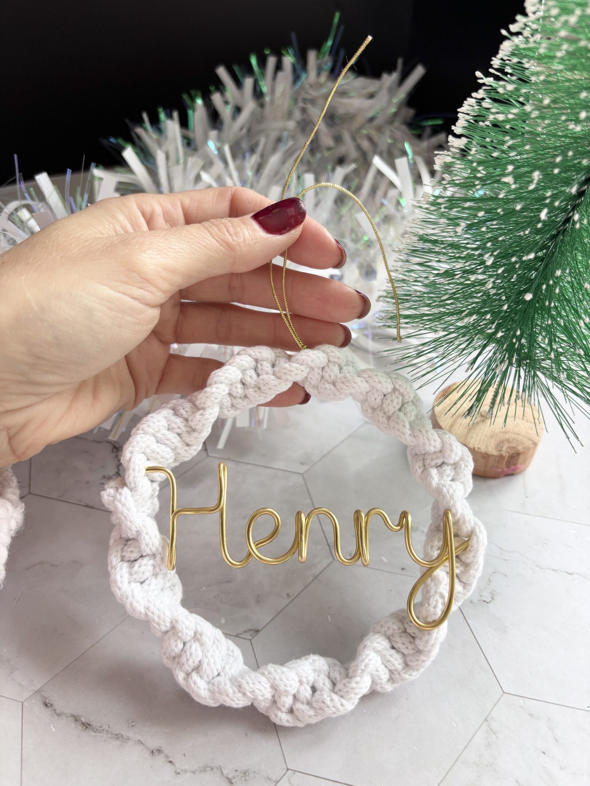 Personalised Christmas tree ornament featuring a white textured wreath and elegant gold wire name lettering, held in hand.
