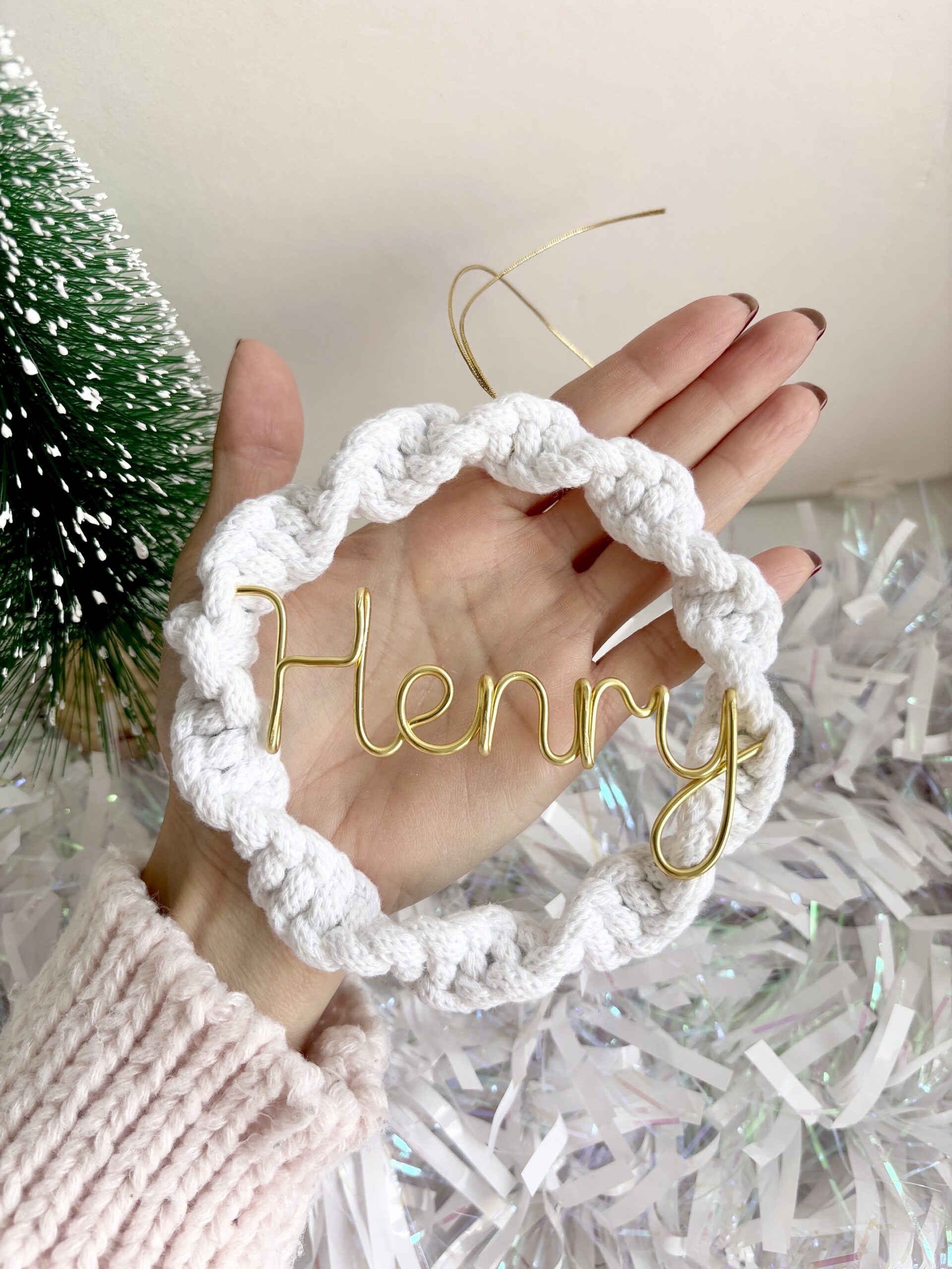 Close-up of a handmade white wreath Christmas ornament with personalised gold wire lettering and a hanging loop.